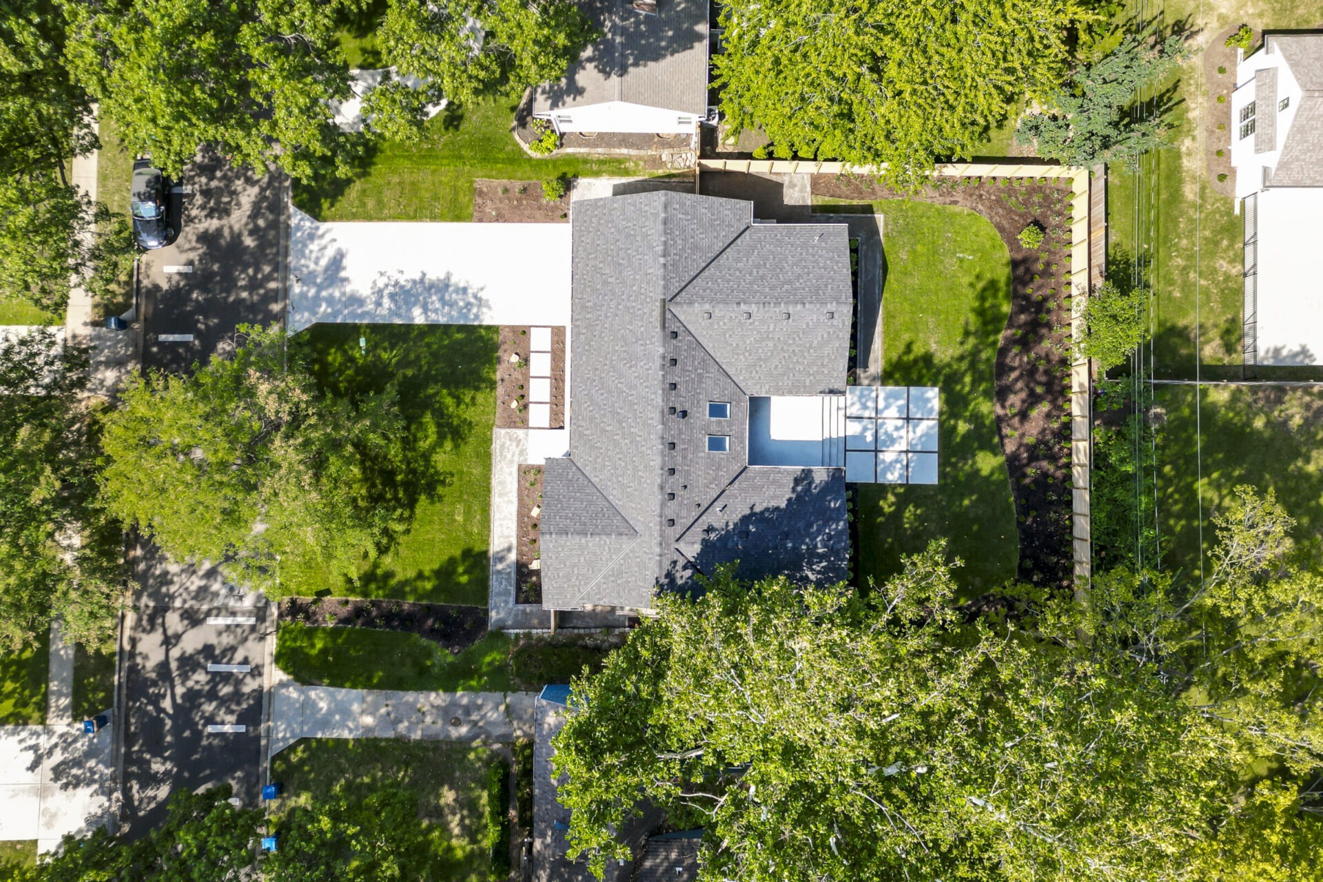 Aerial view of a modern house surrounded by greenery, with a driveway and adjacent street. No landmarks or historical buildings visible.