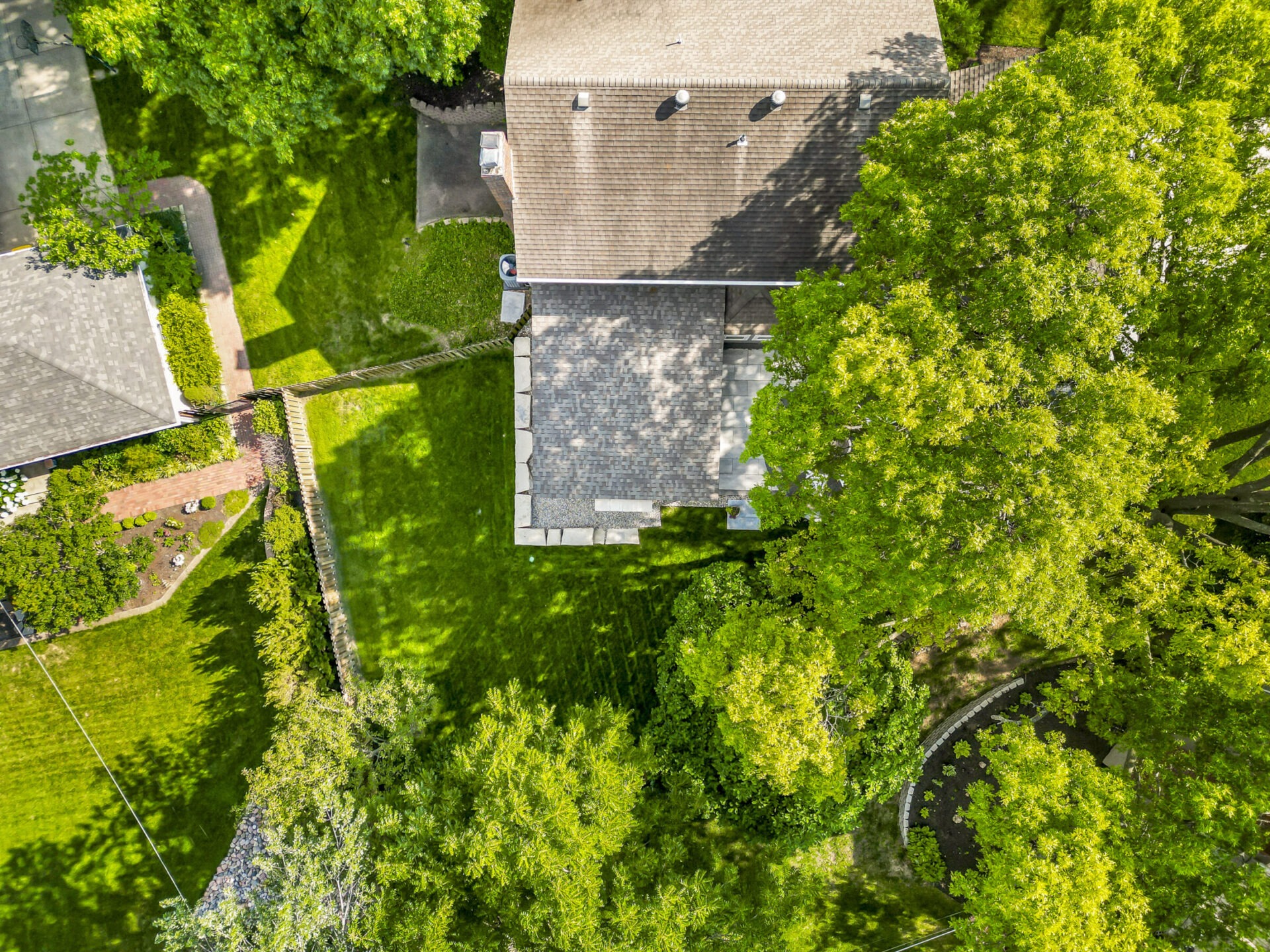 Aerial view of suburban neighborhood with houses, green lawns, and large trees. No recognizable landmarks or historical buildings are visible.