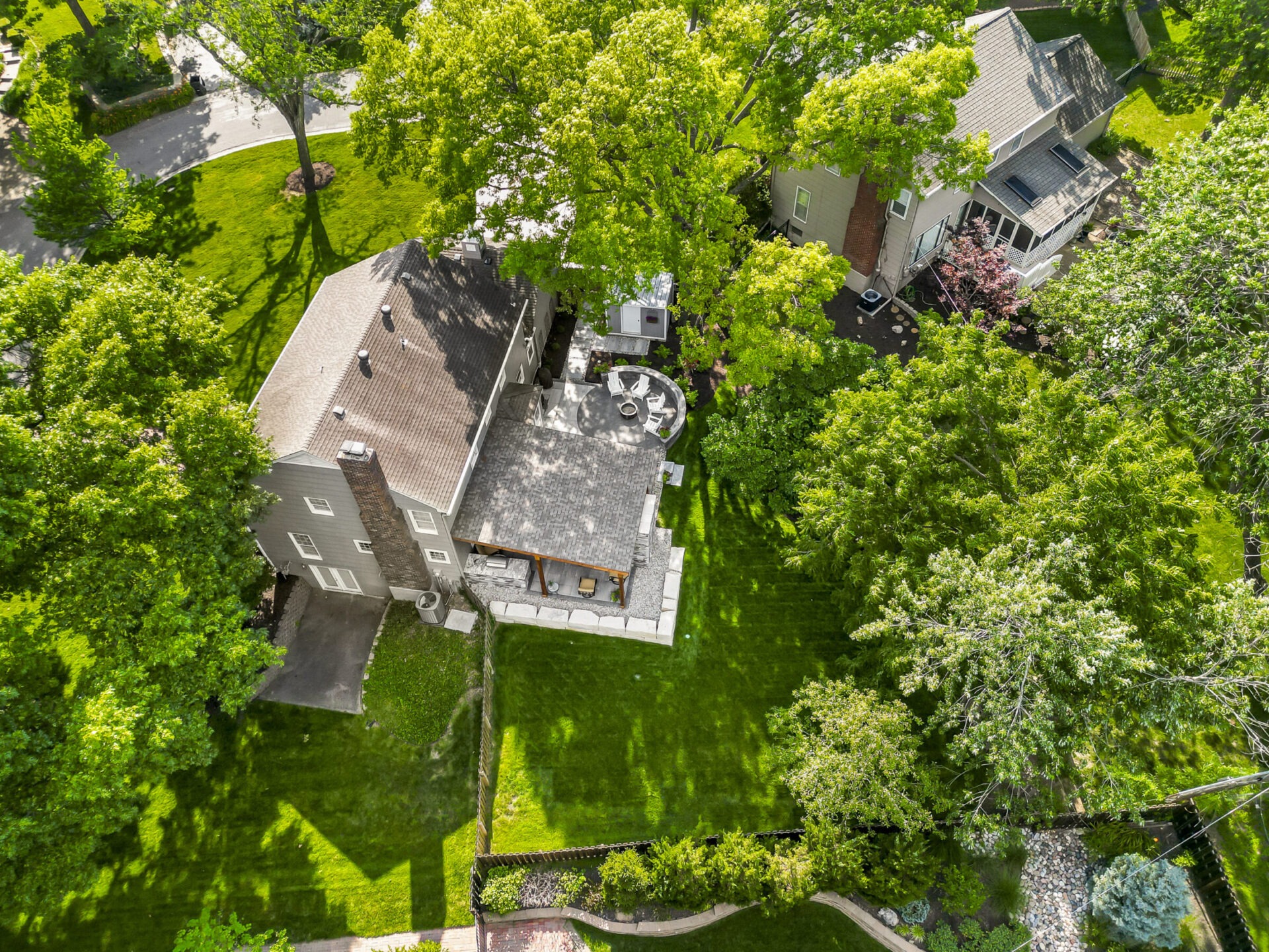 Aerial view of a large house surrounded by lush green trees and lawn, with a visible patio area, on a sunny day.