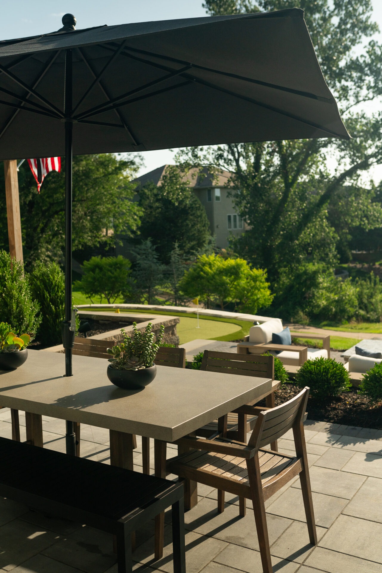 Patio with a table, chairs, and umbrella overlooks a landscaped backyard. U.S. flag is visible, adding a touch of national pride.