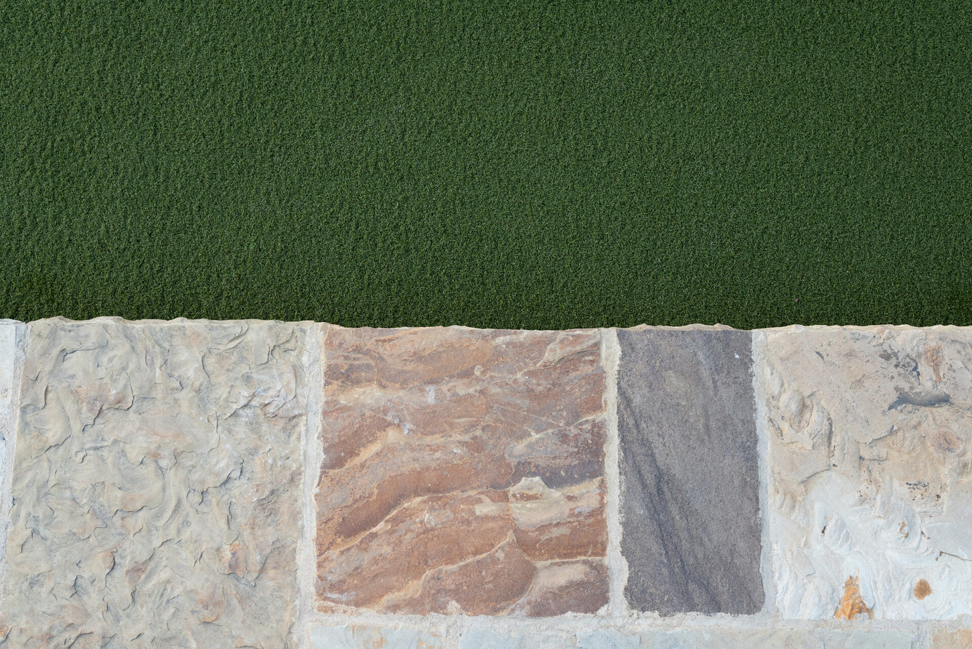 A close-up of a textured stone pathway bordered by a neatly trimmed green lawn, showcasing varied patterns and colors on each stone.