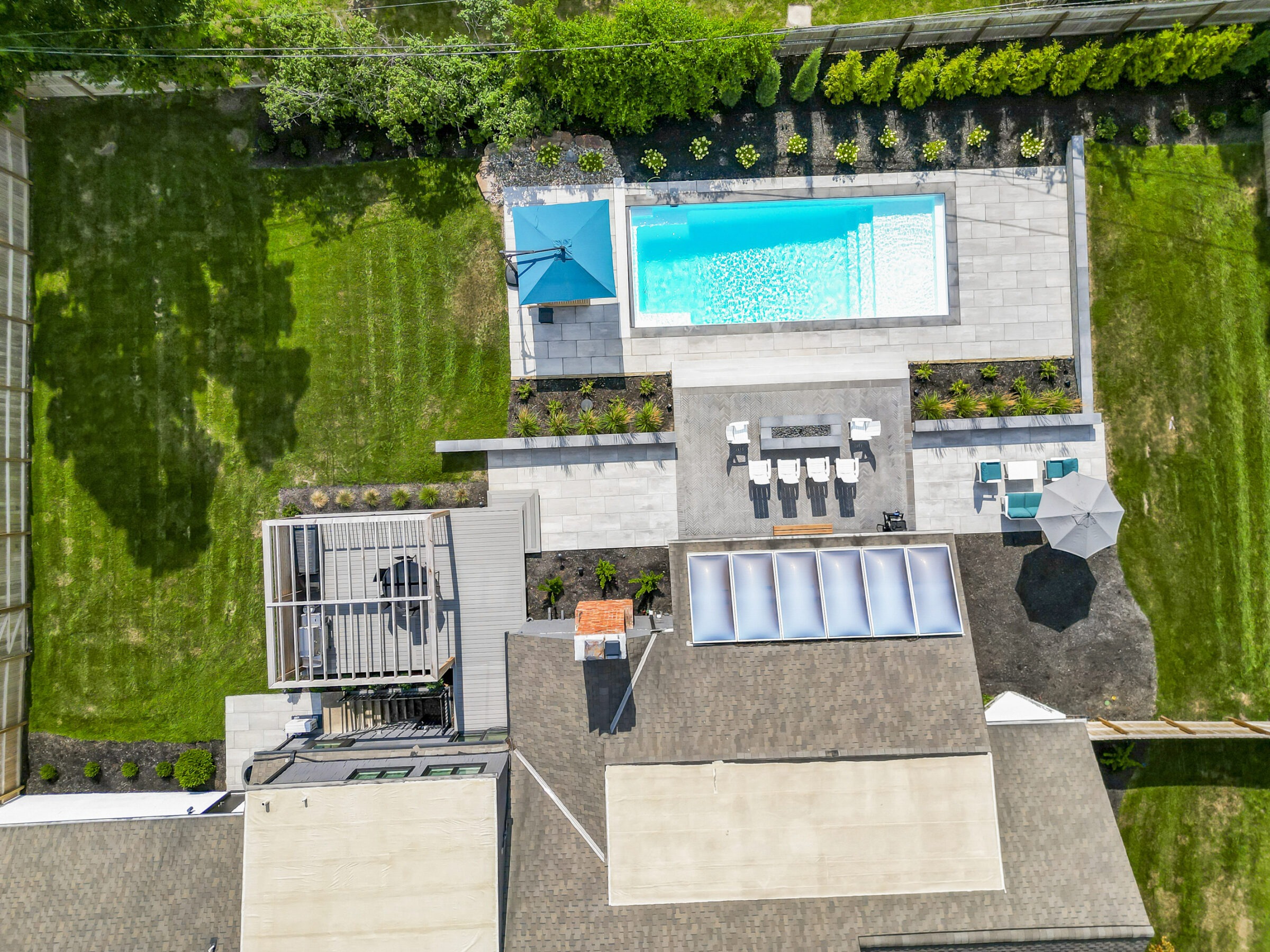 Aerial view of a backyard showcasing a swimming pool, patio with seating, lush grass, and landscaped greenery, creating a serene, modern outdoor space.