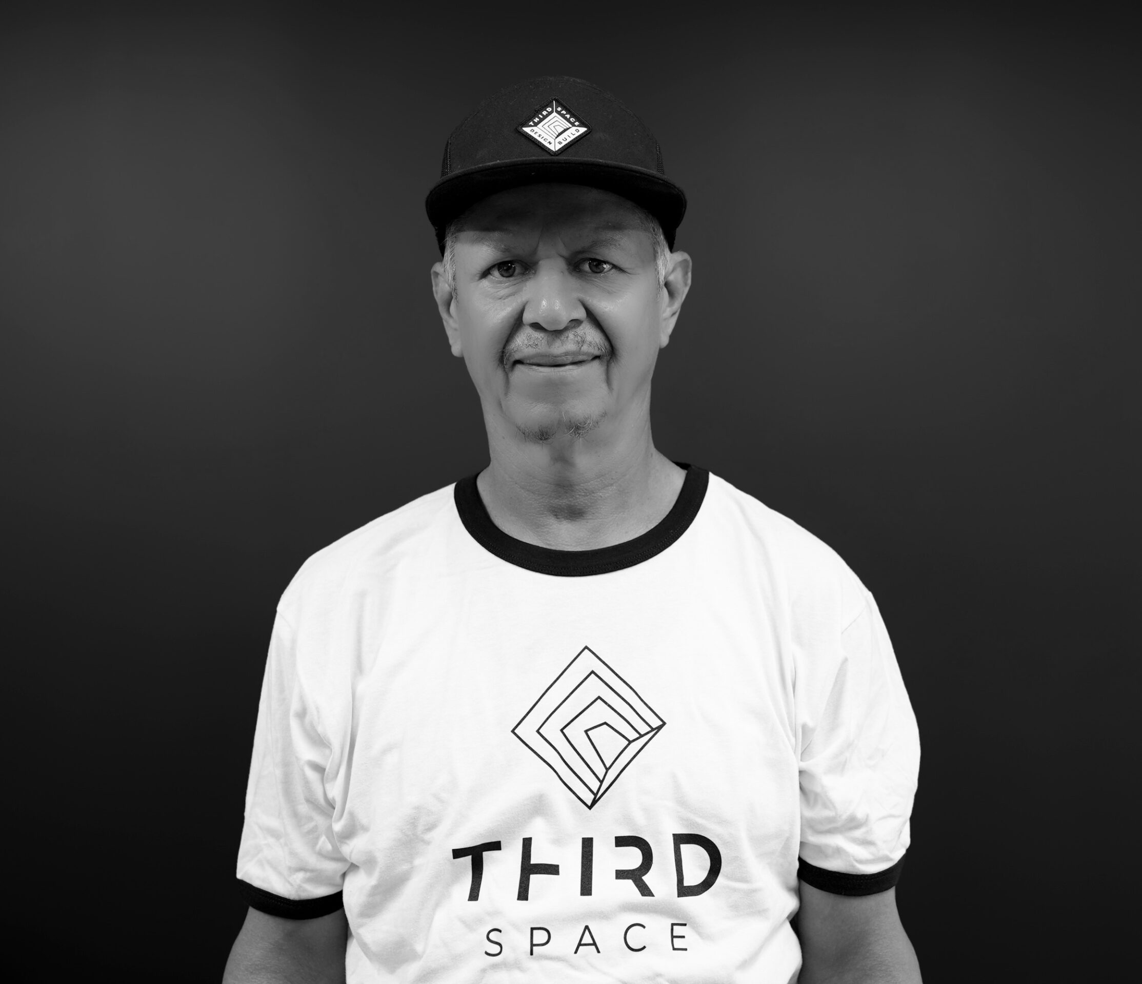 A person wearing a "Third Space" shirt and cap with geometric logo on a plain, dark background, looking directly at the camera.
