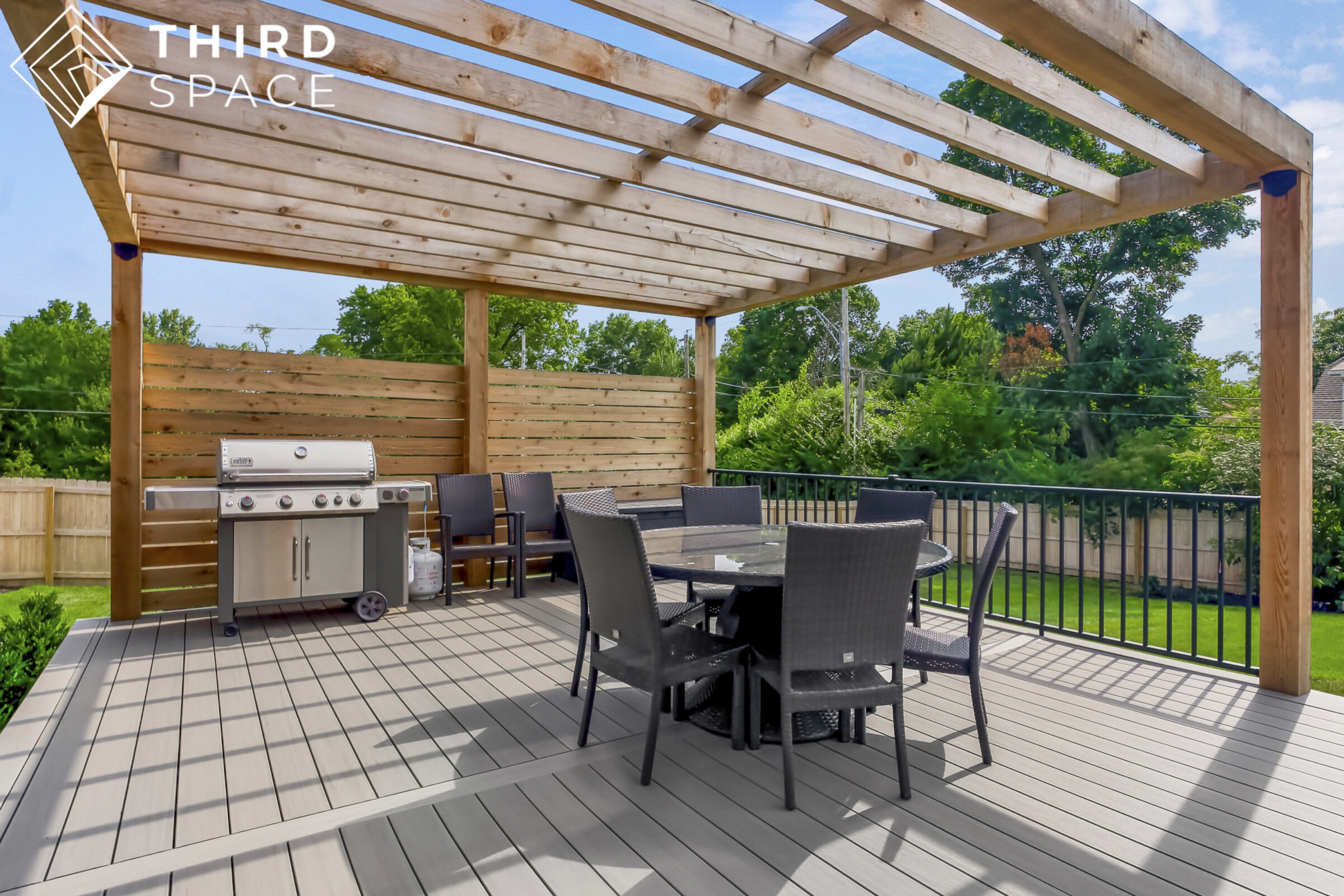 Outdoor patio with pergola, grill, and dining set on a sunny day. Surrounded by lush greenery and wooden fencing, creating a cozy atmosphere.