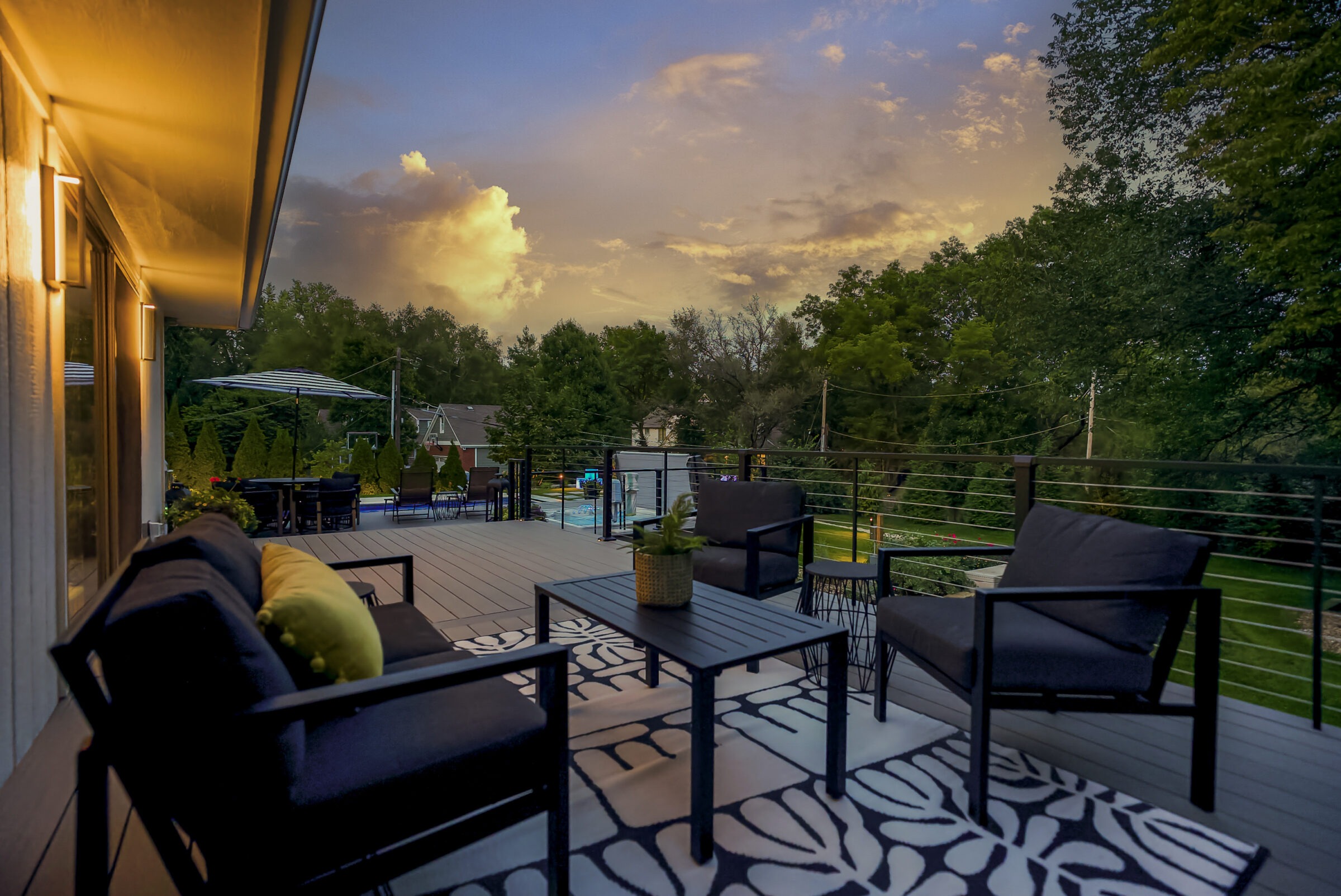 A modern patio with outdoor seating, vibrant sunset sky, and lush trees creates a serene, inviting atmosphere for relaxation and social gatherings.
