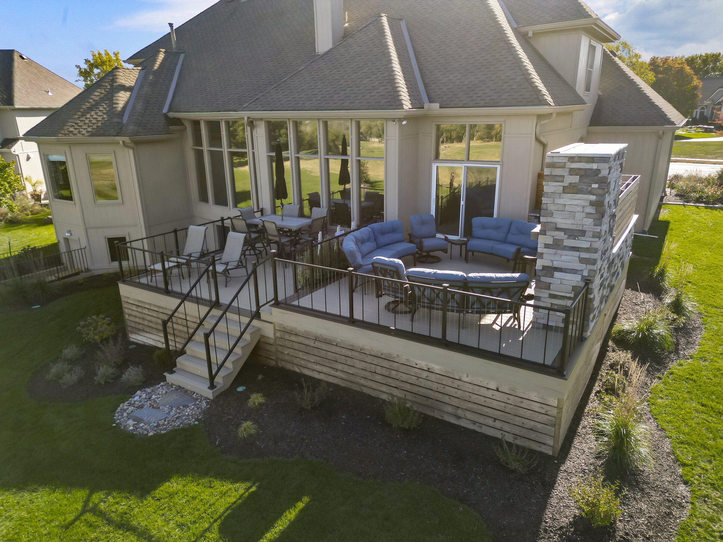 A large house with a spacious patio featuring comfortable seating, a dining area, and decorative landscaping on a sunny day.