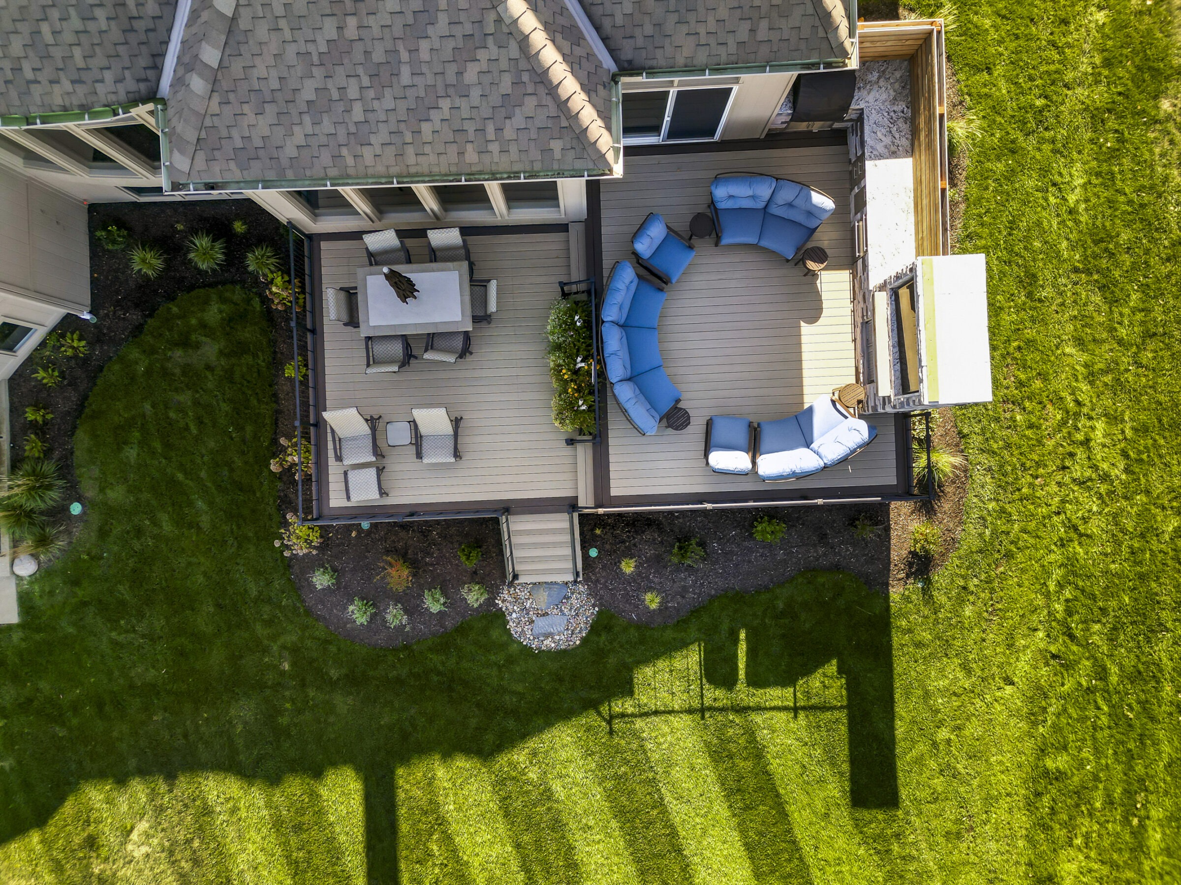 Aerial view of a modern, two-tiered patio with seating and dining areas, surrounded by landscaped greenery and part of a residential home.