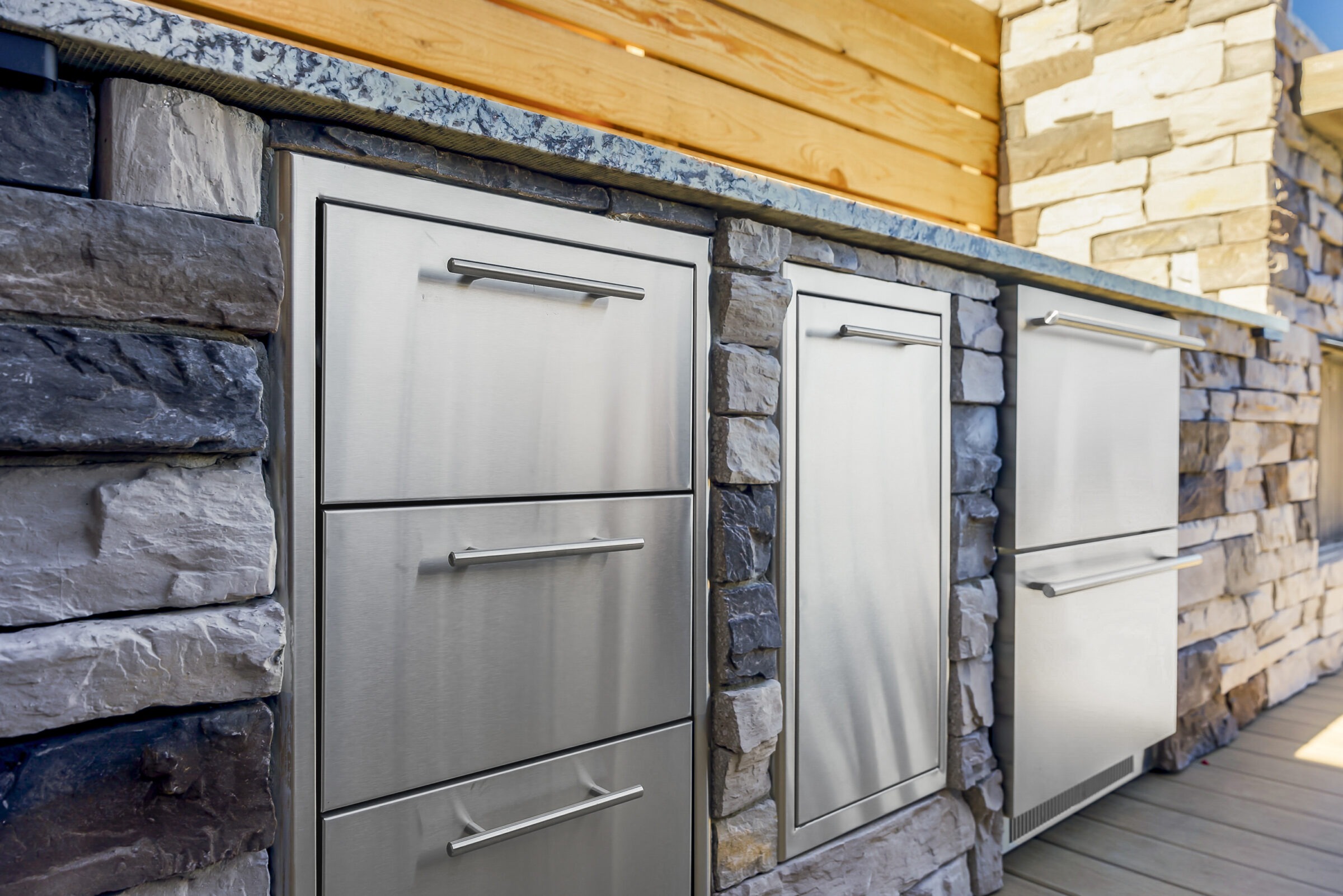 Outdoor kitchen setup featuring elegant stainless steel drawers and appliances set in a stone counter, showcasing modern and rustic design elements.
