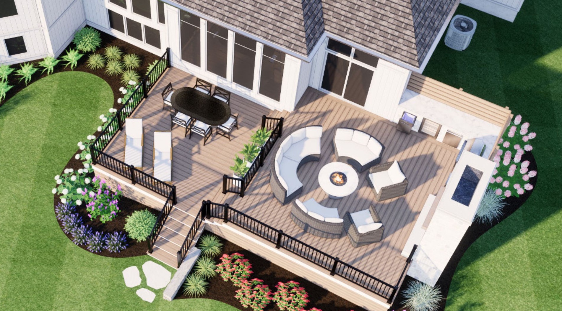 Wooden deck with black railings features a circular seating area, fire pit, dining table, surrounded by lush green garden and colorful flowers.